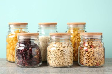 Açık mavi arka planda gri masada farklı ürünler bulunan cam kavanozlar