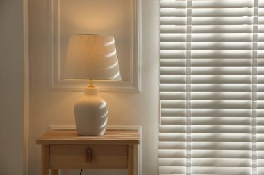 Stylish lamp on nightstand near white wall indoors. Space for text