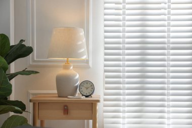 Beyaz duvarın yanındaki komodinin üzerinde şık bir lamba, yüzükler ve çalar saat. Metin için boşluk