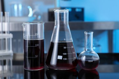 Laboratuvarda kırmızı sıvı bulunan farklı cam eşyalar, yakın plan.