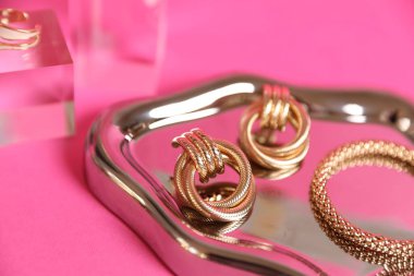 Pembe arka planda güzel altın mücevherlerin şık sunumu, yakın plan.