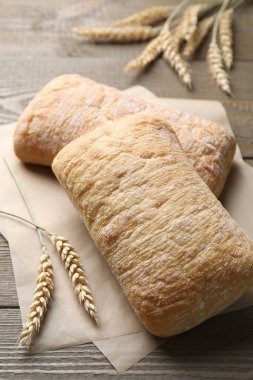 Taze pişmiş ciabatalar ve ahşap masada buğday kulakları, yakın plan.