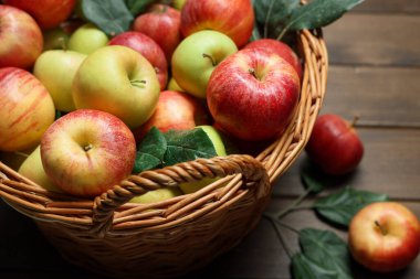 Hasır sepetteki taze elmalar ve yukarıdaki tahta masada yeşil yapraklar.