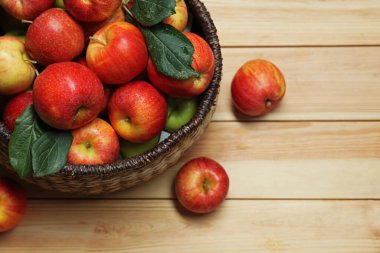 Hasır sepetteki taze elmalar ve ahşap masada yeşil yapraklar, üst manzara. Metin için boşluk