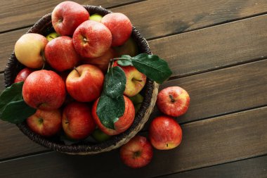 Hasır sepetteki taze elmalar ve ahşap masada yeşil yapraklar, üst manzara. Metin için boşluk