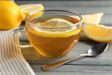 Aromatic tea in cup, lemons and spoon on wooden table, closeup