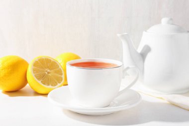 Aromatik çay fincanda, limonlar ve çaydanlık beyaz masada, yakın plan.