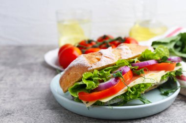 Delicious ciabatta sandwich with prosciutto, cheese and vegetables on light grey table, closeup
