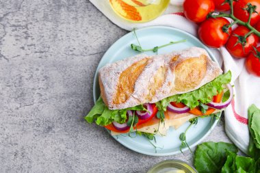 Açık gri masada servis edilen jambonlu, peynirli ve sebzeli nefis ciabatta sandviçi. Metin için boşluk