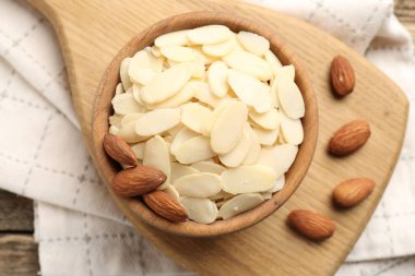 Fresh almond flakes and whole nuts in bowl on table, top view