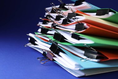 Many folders with documents and binder clips on blue background, closeup