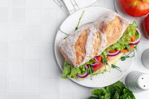 Delicious ciabatta sandwich with prosciutto, cheese and vegetables on white tiled table, flat lay. Space for text