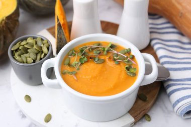 Delicious pumpkin soup with seeds and microgreens in bowl served on table, closeup