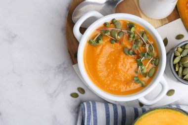 Delicious pumpkin soup with seeds and microgreens in bowl served on white marble table, flat lay. Space for text