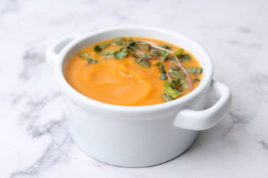 Delicious pumpkin soup with seeds and microgreens in bowl on white marble table, closeup