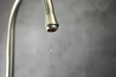 Su tasarrufu konsepti. Gri arka planda musluktan su damlıyor, yakın plan. Metin için boşluk