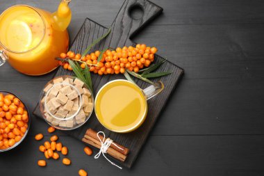 Bardakta deniz dikenli çay, çaydanlık, taze böğürtlen, kahverengi şeker ve tarçın siyah ahşap masa, düz yatak. Metin için boşluk