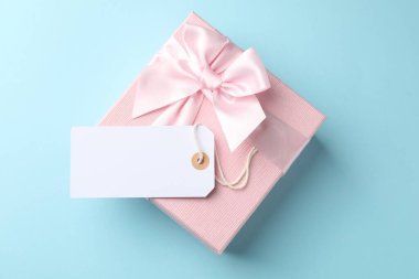 Blank tag and gift box on light blue background, top view