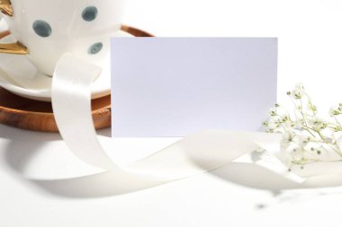 Beyaz arka planda boş kart, kurdele, bardak ve güzel çiçekler, yakın plan.