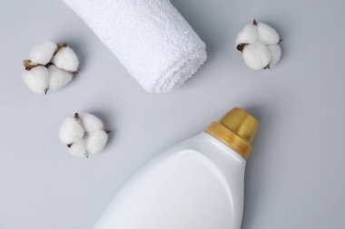 Bir şişe yumuşatıcı, havlu ve pamuk çiçekleri açık gri arka planda, düz yatıyordu.