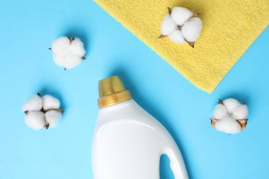 Bir şişe yumuşatıcı, havlu ve pamuk çiçekleri açık mavi arka planda, düz yerde.