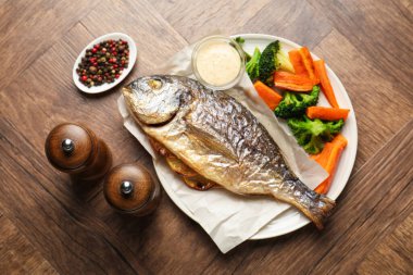 Tuz, karabiber değirmeni, lezzetli kızarmış dorado balığı, sebze, sos ve biberler ahşap masada, düz uzanmış