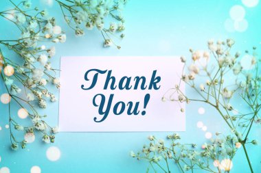 Thank you card and flowers on light blue background, top view. Bokeh lights