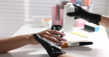 Salondaki masada yapılan manikür ameliyatından sonra müşterinin eline talk pudrası serpiştiren bir kadın. Kamera içeri giriyor.