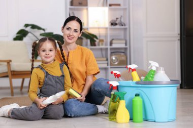 Küçük yardımcı. Evde farklı temizlik ürünleri ve malzemeleriyle anne ve kızı var.