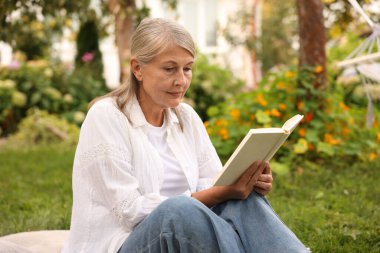 Yeşil çimenler üzerine kitap okuyan son sınıf öğrencisi kadın.