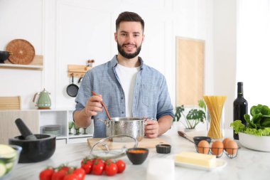 Mutfaktaki masada yemek pişiren gülümseyen adam.