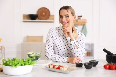 Mutfaktaki masada yemek yapan gülümseyen kadının portresi.