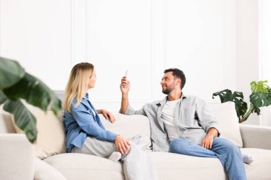Evdeki koltukta uzaktan kumandayla klima kullanan çift.