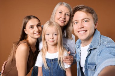 Kahverengi arka planda annesi ve ailesiyle selfie çeken bir adam.