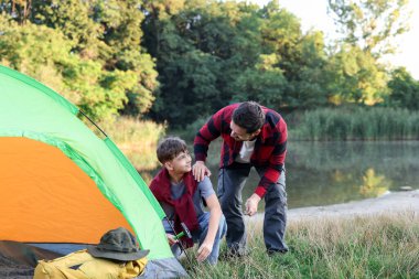 Baba ve oğul nehir kenarında kamp çadırı kuruyorlar.