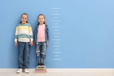 Mavi duvarın yanında boylarını ölçen küçük kızlar.