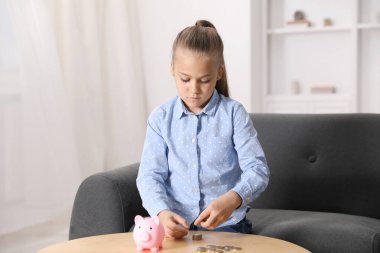 Küçük kız içeride ahşap masada cep harçlığını sayıyor.