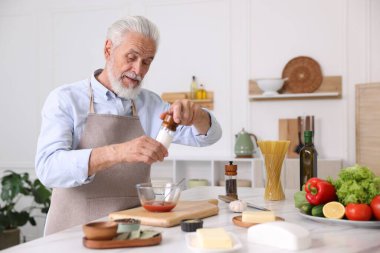 Mutfaktaki beyaz mermer masada yaşlı bir adam yemek pişiriyor.