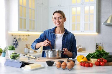 Mutfaktaki masada yemek yapan gülümseyen kadın.