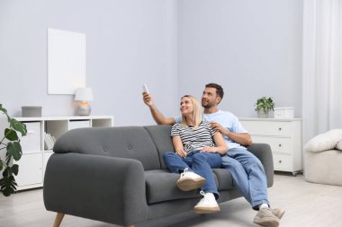 Evdeki koltukta uzaktan kumandayla klima kullanan çift.