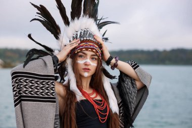 Kızılderili başlıklı güzel bir şaman kadın. Yüzü boyalı ve dışarıda nehir kenarında mücevherleri var.