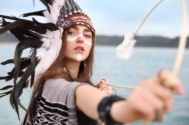 Kızılderili başlıklı güzel bir kadının portresi. Yüzü boyalı, ok ve yay açık nehir kenarında.