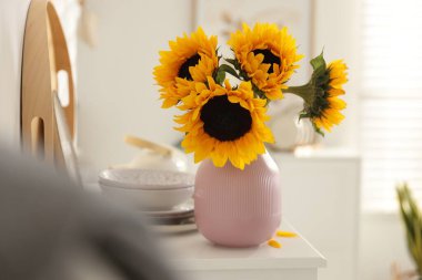 Vazodaki güzel ayçiçekleri ve evdeki beyaz çekmecelerin üstündeki mutfak gereçleri