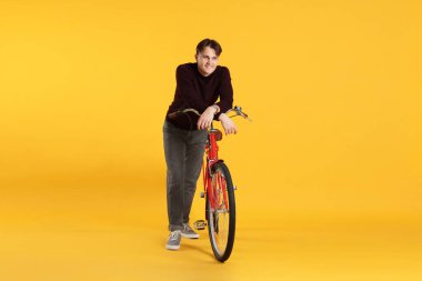 Turuncu arka planda kırmızı bisikletli yakışıklı bir adam.