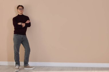 Bej duvarın yanında şık kotlu bir adam.