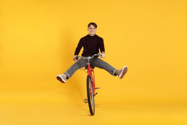 Turuncu arka planda kırmızı bisiklet süren yakışıklı bir adam.