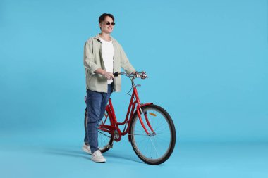 Açık mavi arka planda kırmızı bisikletli yakışıklı bir adam.
