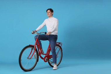 Açık mavi arka planda kırmızı bisiklete binen yakışıklı adam, metin için boşluk