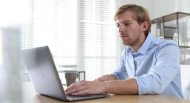 İçerideki ahşap masada dizüstü bilgisayar kullanan adam.