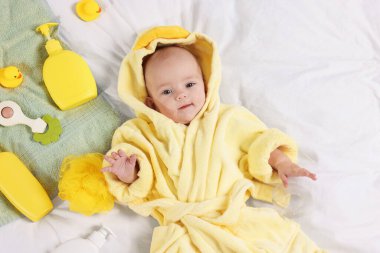 Yatakta banyo aksesuarları ve bornozlu şirin bir bebek.